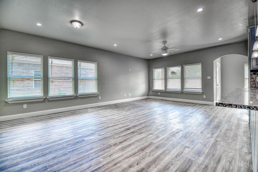 Unfurnished living room featuring a healthy amount of sunlight, ceiling fan, hardwood / wood-style flooring, and a textured ceiling