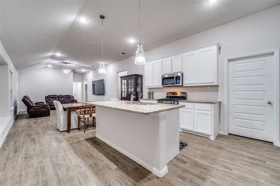 Kitchen with stainless steel appliances, vaulted ceiling, pendant lighting, white cabinets, and an island with sink