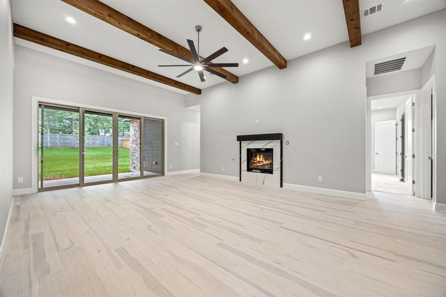 Unfurnished living room featuring beam ceiling, a fireplace, light wood-type flooring, and ceiling fan