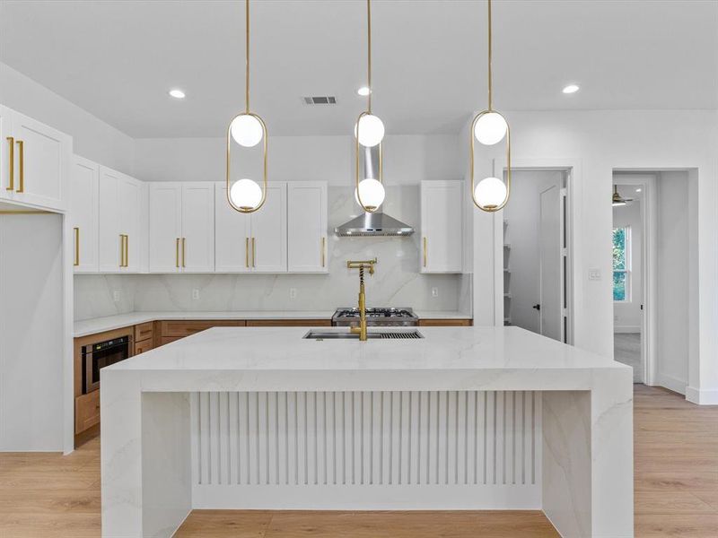 Kitchen featuring an island with sink, white cabinets, and hanging light fixtures