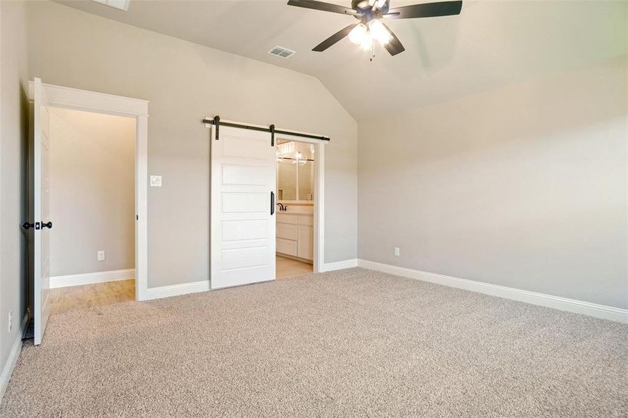 Unfurnished bedroom featuring ensuite bath, ceiling fan, a barn door, and light colored carpet