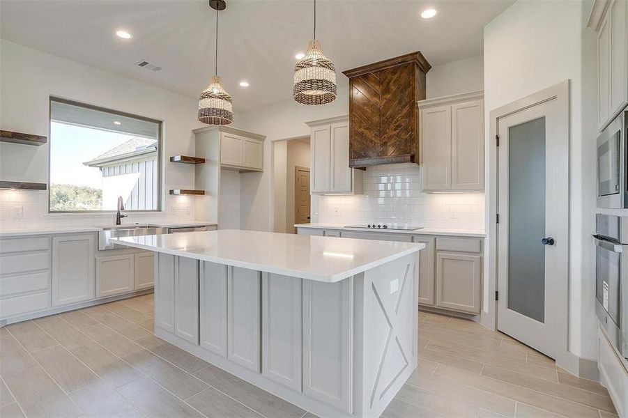 Kitchen featuring decorative backsplash, appliances with stainless steel finishes, a center island, sink, and decorative light fixtures