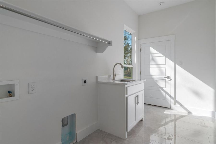 Washroom with hookup for an electric dryer, light tile patterned floors, hookup for a washing machine, cabinets, and sink