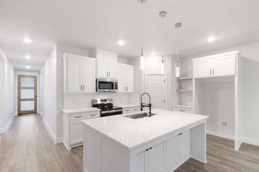 Kitchen featuring white cabinets, appliances with stainless steel finishes, a kitchen island with sink, and sink