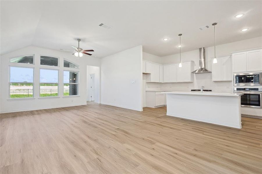 Kitchen with white cabinets, wall chimney exhaust hood, stainless steel appliances, and light hardwood / wood-style flooring