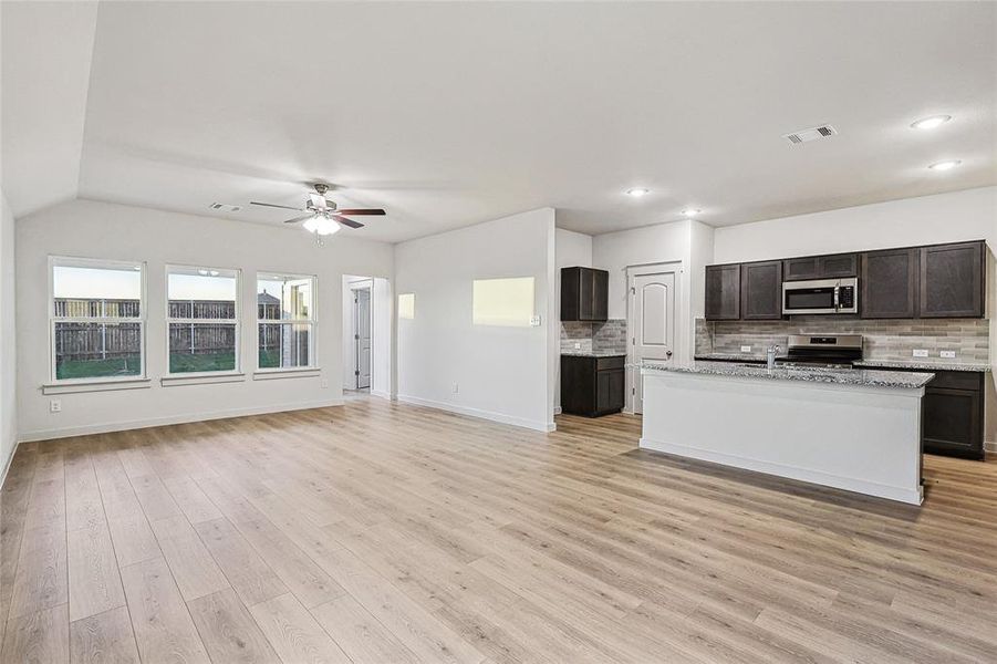 Kitchen with light hardwood / wood-style floors, tasteful backsplash, an island with sink, appliances with stainless steel finishes, and ceiling fan