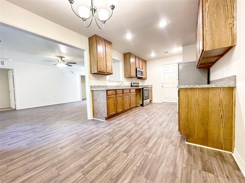 Kitchen with ceiling fan with notable chandelier, pendant lighting, stainless steel appliances, light wood-type flooring, and sink