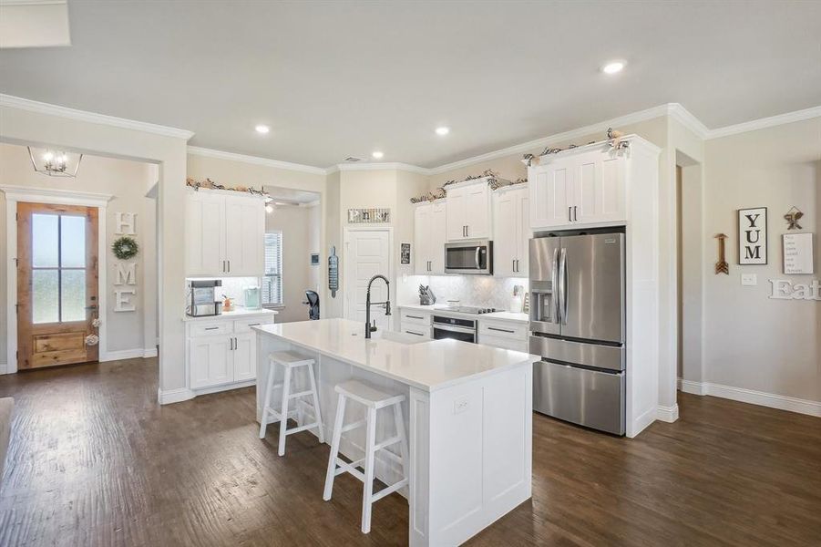 Kitchen featuring white cabinets, a kitchen island with sink, appliances with stainless steel finishes, and dark wood-type flooring