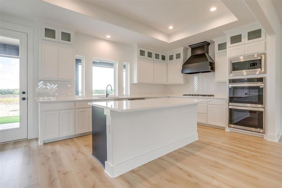 Kitchen featuring a healthy amount of sunlight, appliances with stainless steel finishes, premium range hood, and white cabinetry