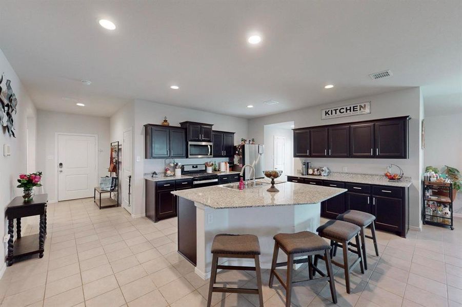 Kitchen featuring a kitchen breakfast bar, a kitchen island with sink, light tile floors, and stainless steel appliances