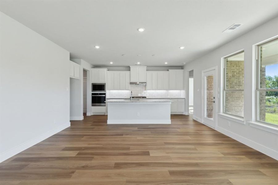 Kitchen featuring white cabinets, tasteful backsplash, a center island with sink, light hardwood / wood-style flooring, and stainless steel appliances