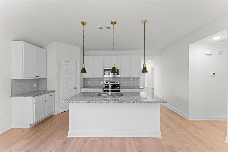 Kitchen with white cabinetry, a kitchen island with sink, stainless steel appliances, and hanging light fixtures