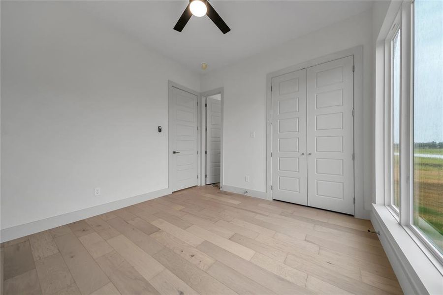 Unfurnished bedroom featuring light hardwood / wood-style floors, multiple windows, ceiling fan, and a closet