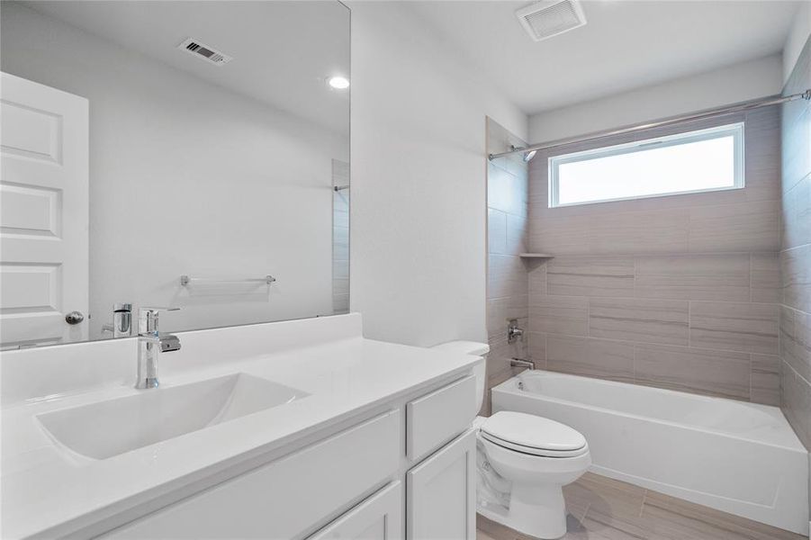 Secondary bathroom features light countertops and cabinets, neutral paint, shower/tub combo with tile surround, large mirror, tile floors, sleek fixtures and modern finishes.