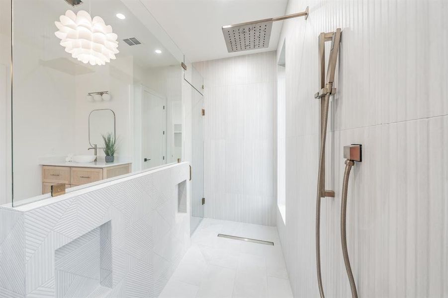 Bathroom featuring designer tiled shower, vanity, and marble-like tile flooring