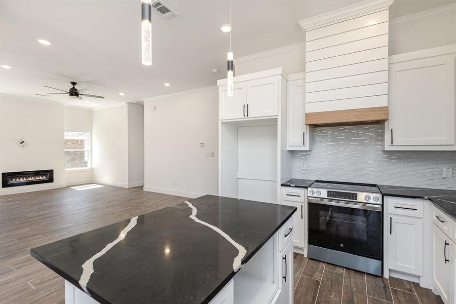 Kitchen with white cabinets, dark wood-type flooring, stainless steel stove, and decorative light fixtures