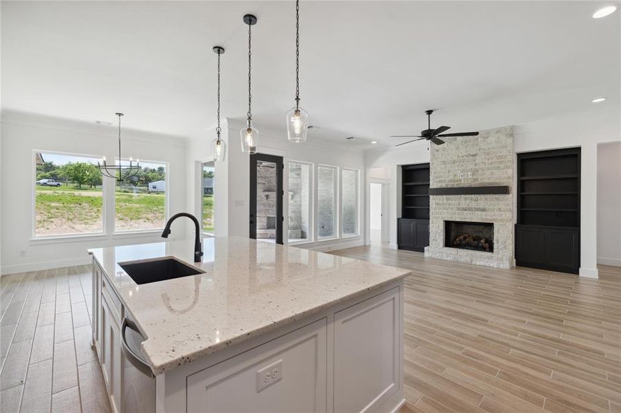 Kitchen with a fireplace, ceiling fan with notable chandelier, light stone counters, sink, and a kitchen island with sink