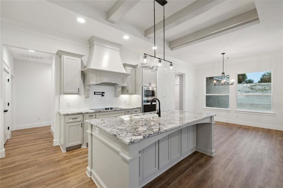 Kitchen with custom range hood, stainless steel appliances, hardwood / wood-style floors, decorative backsplash, and a center island with sink