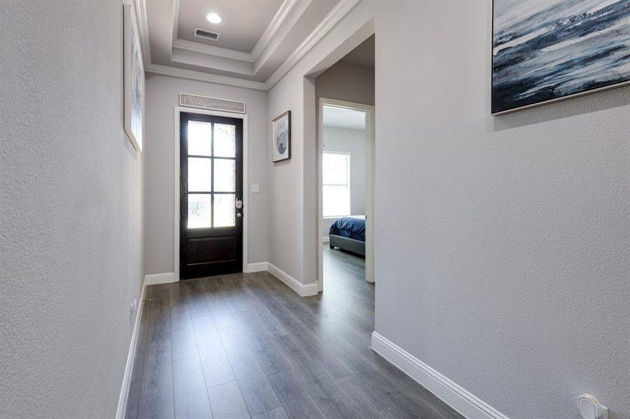 Entrance foyer with a tray ceiling, ornamental molding, and dark wood-type flooring