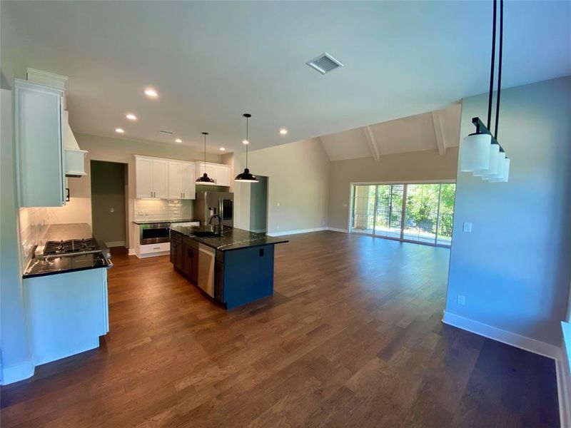 Kitchen featuring an island with sink, vaulted ceiling with beams, pendant lighting, and dark wood-type flooring