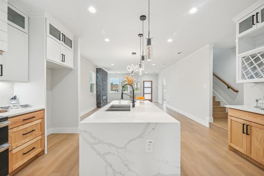 Kitchen with white cabinets, light brown cabinetry, decorative light fixtures, sink, and a center island with sink