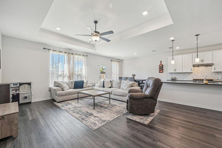 Living room featuring dark wood-type flooring, a tray ceiling, and ceiling fan