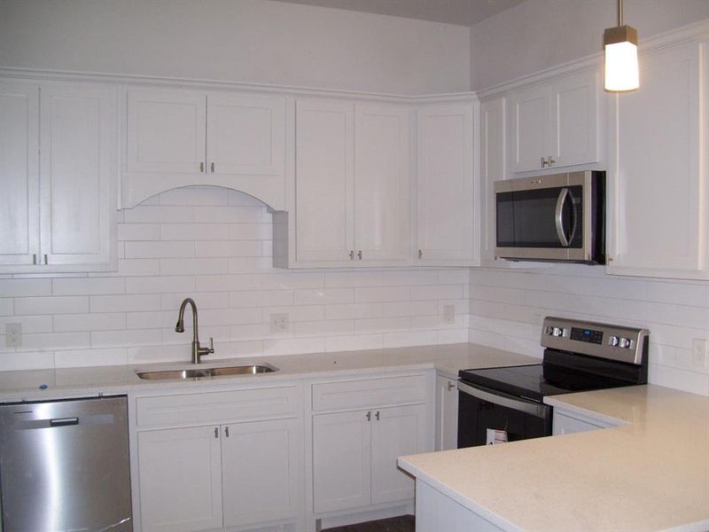 Kitchen featuring quartz countertops, subway tile backsplash, custom cabinetry and stainless steel appliances