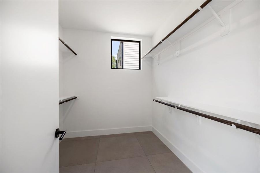 This is a clean, well-lit walk-in closet with multiple shelves and hanging rods for storage, featuring a small window for natural light.