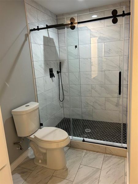 Bathroom featuring toilet, tile floors, and a shower with door