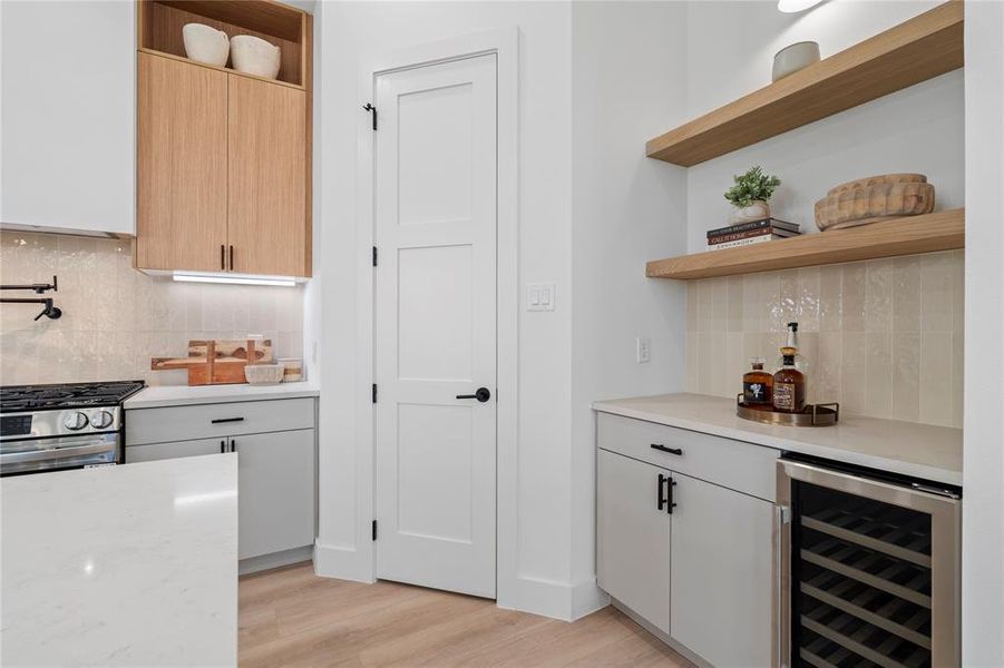 This well-appointed kitchen corner features both a built-in wine cooler and sleek open shelving, making it the ideal spot for entertaining. The addition of a convenient pot filler above the stove enhances the kitchen’s functionality, catering to culinary enthusiasts while maintaining a polished, modern aesthetic. Perfect for those who love to cook and entertain with ease.