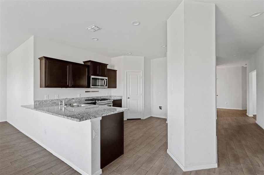 Kitchen with light hardwood / wood-style floors, sink, kitchen peninsula, light stone counters, and appliances with stainless steel finishes