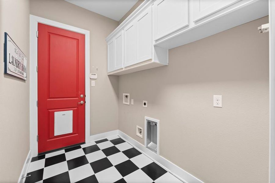 This laundry room is ready to be used to support the household with whimsical charm featuring black and white checkered flooring and a red door entrance to the garage (featuring a large doggie door).