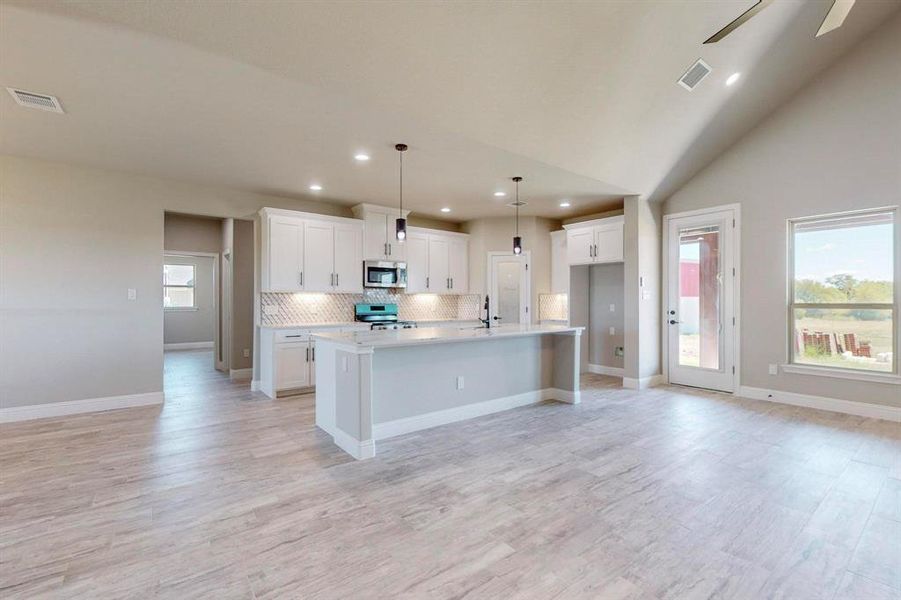 Kitchen featuring ceiling fan, white cabinets, an island with sink, and stainless steel appliances