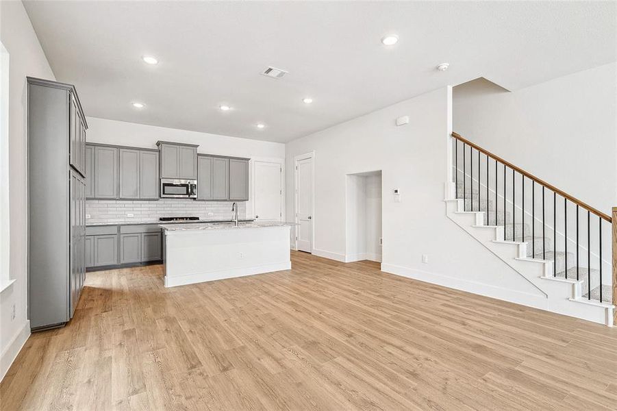 Kitchen with backsplash, light hardwood / wood-style floors, sink, gray cabinetry, and a kitchen island with sink