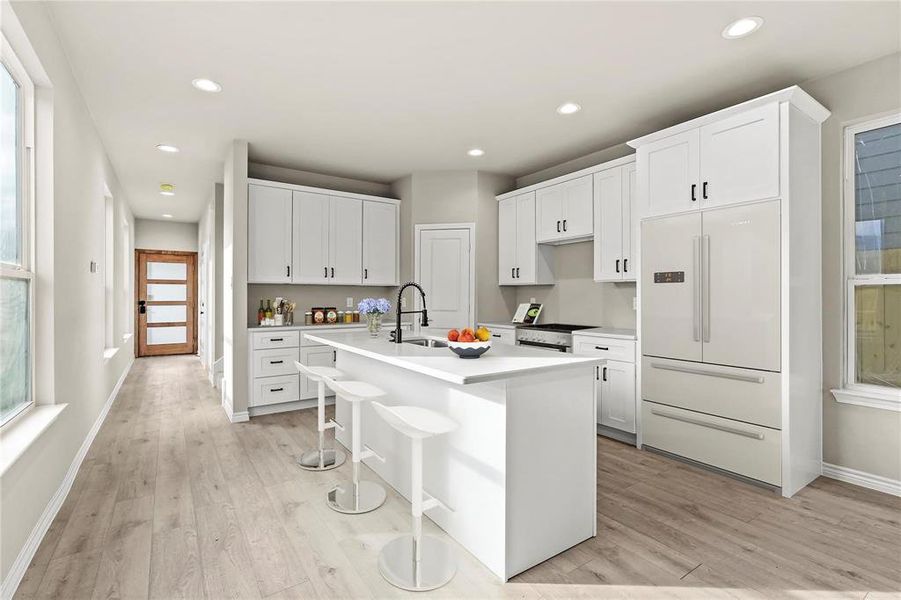 Kitchen featuring a kitchen bar, light hardwood / wood-style floors, a center island with sink, built in refrigerator, and white cabinets