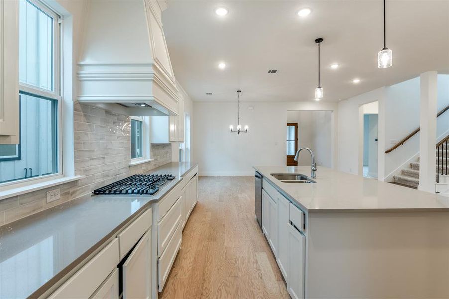 Kitchen with custom range hood, a kitchen island with sink, sink, backsplash, and light hardwood / wood-style flooring