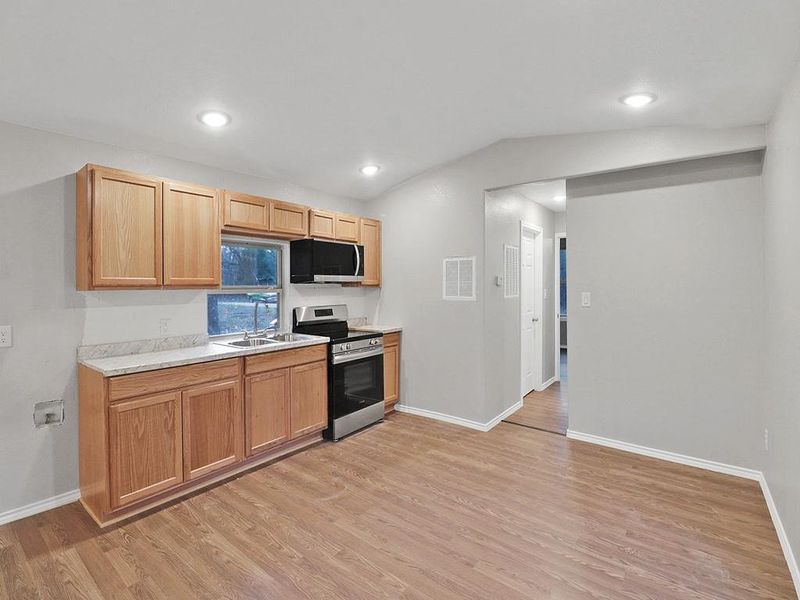 Kitchen featuring light hardwood / wood-style flooring, lofted ceiling, appliances with stainless steel finishes, and sink