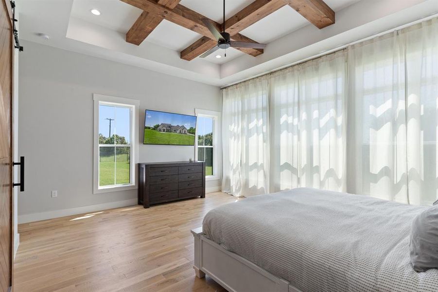 Bedroom featuring light wood-type flooring, beamed ceiling, a barn door, coffered ceiling, and ceiling fan