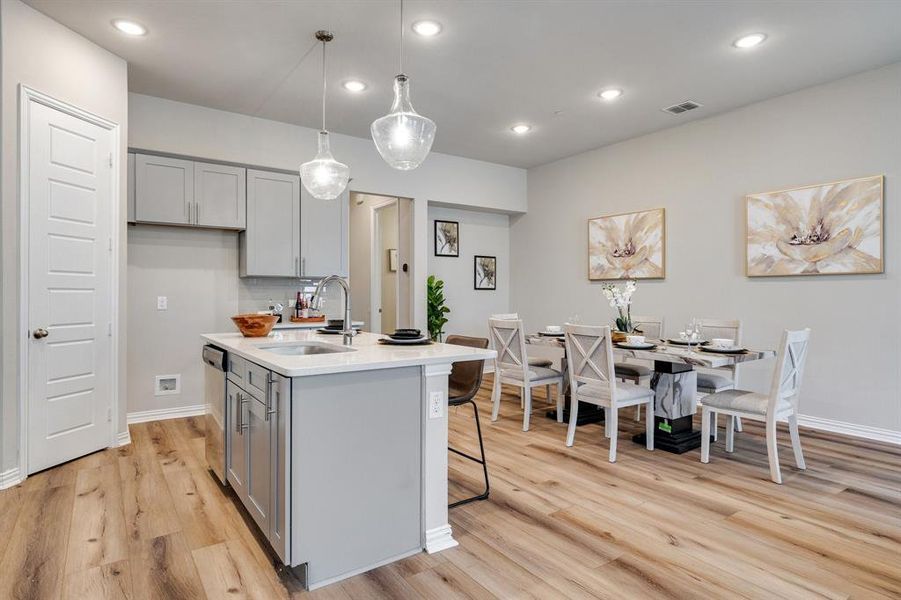 Kitchen featuring sink, decorative light fixtures, a kitchen island with sink, light hardwood / wood-style flooring, and gray cabinets