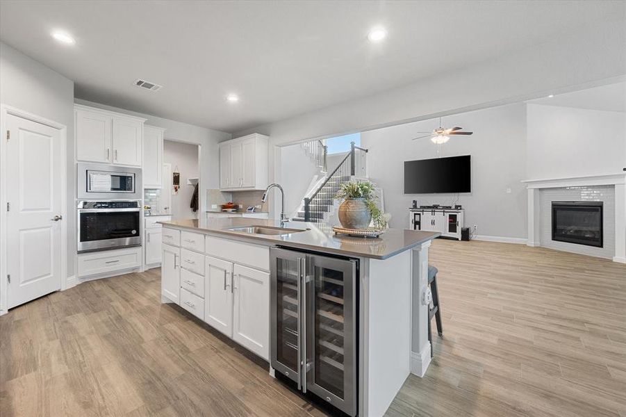 Kitchen featuring wine cooler, sink, a kitchen island with sink, white cabinetry, and stainless steel appliances