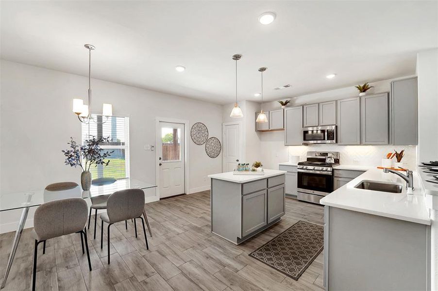 Kitchen with sink, decorative light fixtures, gray cabinets, appliances with stainless steel finishes, and light wood-type flooring