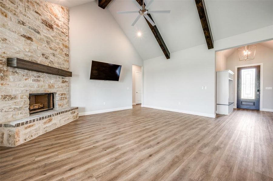 Unfurnished living room with a stone fireplace, hardwood / wood-style floors, and beam ceiling