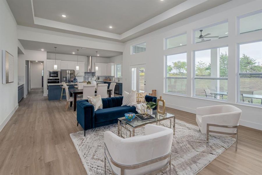 Living room featuring light wood flooring, ceiling fan, plenty of natural light, and a raised ceiling