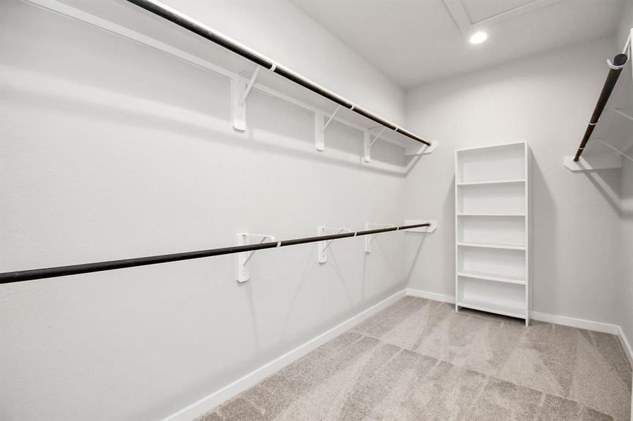 Experience luxury in this spacious walk-in closet with high ceilings and plush carpet. Warm paint tones, built-in shelving, and dark finishes create a contemporary and functional retreat. Sample photo of completed home with similar floor plan. As-built interior colors and selections may vary.