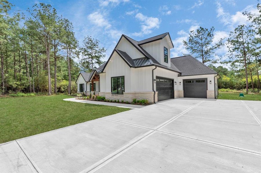 A clean, white exterior with contrasting dark roof and garage doors, a spacious concrete driveway, and a welcoming front lawn set against a backdrop of mature trees.