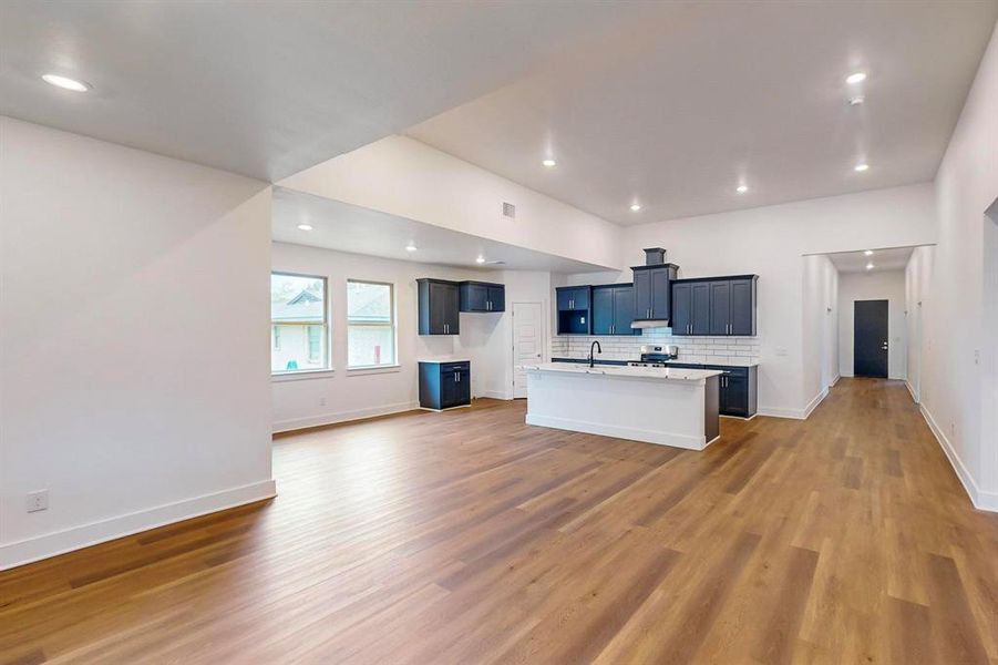 Kitchen featuring backsplash, custom range hood, dark hardwood / wood-style flooring, sink, and an island with sink