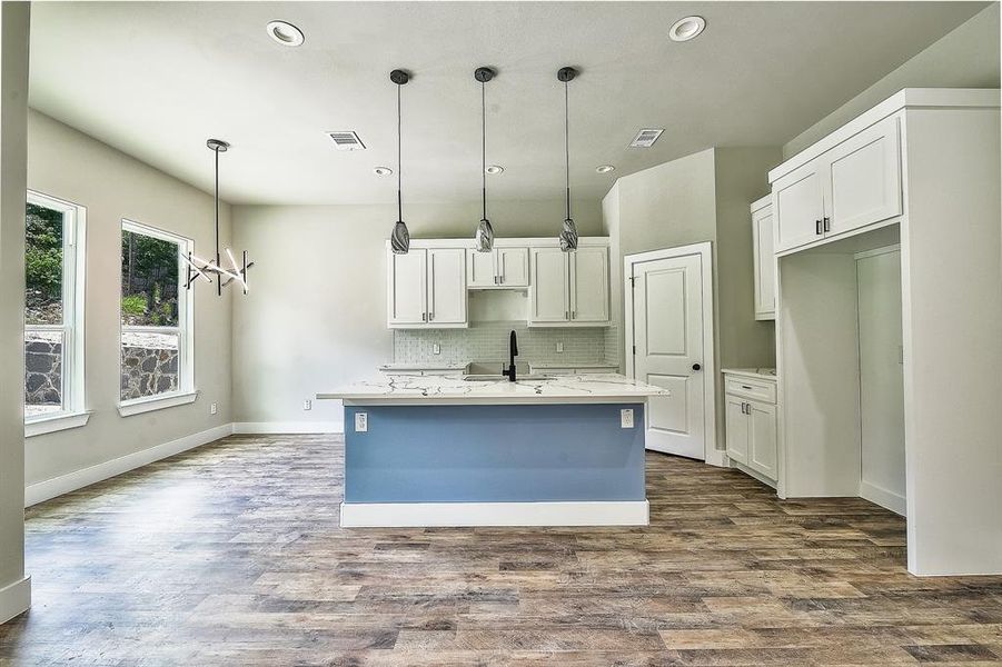 Kitchen featuring an island with sink, white cabinets, hardwood / wood-style floors, backsplash, and pendant lighting