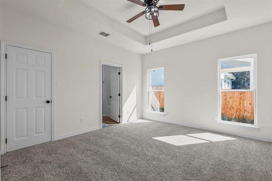 Unfurnished bedroom featuring a raised ceiling, ceiling fan, and carpet floors