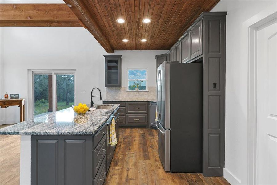 Kitchen featuring stainless steel appliances, dark wood-type flooring, light stone countertops, and backsplash