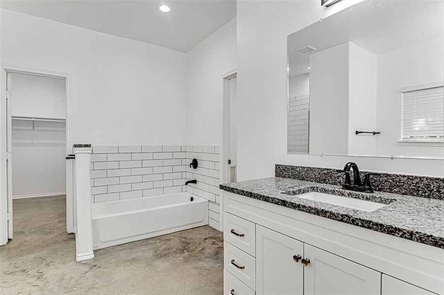 Bathroom featuring concrete floors, vanity, and a tub to relax in